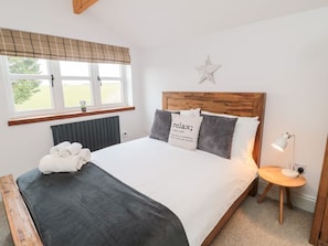 A bedroom with a bed, a bedside table with a lamp, a window with blinds, and a star decoration on the wall. - Canny Cottage: A Pet-Friendly Retreat (Belford)