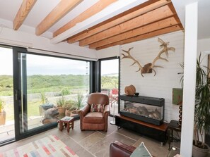 Ein modernes Wohnzimmer mit Kamin, Ledersessel und großen Fenstern mit Blick auf eine grüne Landschaft.