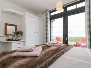 Ein Schlafzimmer mit großem Fenster, einem Bett mit brauner, flauschiger Decke und Blick ins Freie.
