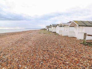 A pebbled beach with white beach huts aligned along the shore.
