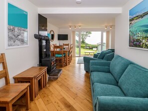 A living room with a sofa, wooden furniture, a fireplace, and a TV. - 3 Moranedd, Moelfre, Anglesey. (Moelfre)