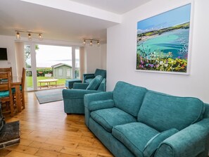 A living room with a teal sofa, a wooden coffee table, and a painting of a landscape. - 3 Moranedd, Moelfre, Anglesey. (Moelfre)