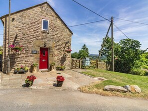 A stone building with a red door, stone walls, and a grassy area with a view of the landscape. - The Old Chapel, Crich (Matlock)
