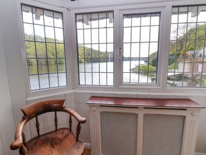 Ein Zimmer mit Blick auf einen See durch drei Fenster, ein Holzstuhl und eine Heizung.