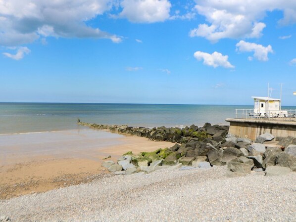 A beach with a rocky breakwater, calm sea, and a lifeguard tower.