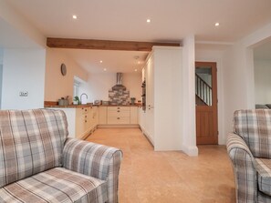 A modern kitchen with a central island, wooden beams, and a staircase leading to a second floor. - Vine Cottage, Pilling (Preston)