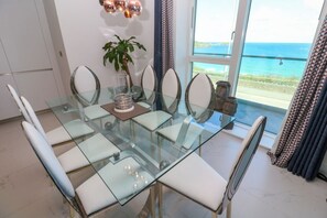A dining area with a glass table and chairs, a potted plant, and a view of the ocean through a large window. - 17 Cliff Edge Newquay Cornwall (Newquay)