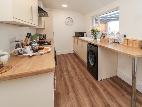 A kitchen with wooden countertops, a washing machine, and a clock on the wall.