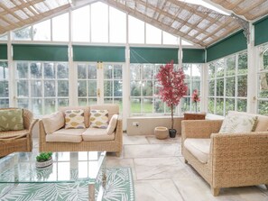 A conservatory with wicker furniture, a glass table, and a potted plant.