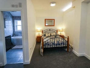 Ein Schlafzimmer mit einem Bett, Nachttischlampen, einem Spiegel und Blick ins Badezimmer.