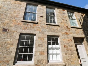 Ein Steinhaus mit drei Fenstern, jeweils mit weißen Rahmen und mehreren Glasscheiben.