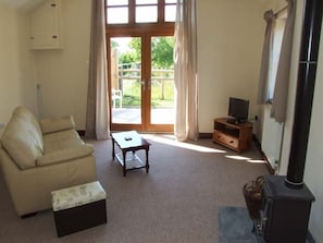 A living room with a sofa, a table, a television on a stand, a fireplace, and a sliding glass door leading outside. - Dovetail , Westbury-On-Severn (Gloucester)