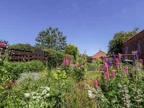 Un jardín con diversas plantas y flores, un edificio de ladrillo y una estructura de madera.