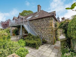 A stone building with a staircase leading to a balcony, surrounded by greenery.
