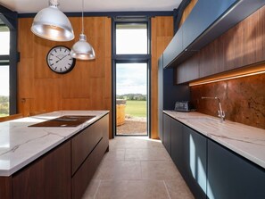 A modern kitchen with wooden cabinetry, a marble countertop, pendant lighting, and a view through the glass door. - Brock House, in Northallerton. (Northallerton)