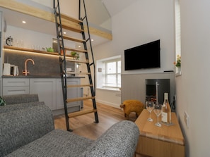 A modern living room with a fireplace, a television mounted on the wall, and a wooden table with glasses. - Llofft Penwaig (The Herring Loft) (Cemaes Bay)
