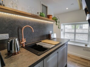 A modern kitchen with a copper faucet, a kettle, a toaster, and a wooden cutting board on the counter. - Llofft Penwaig (The Herring Loft) (Cemaes Bay)