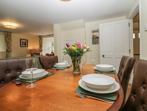 A dining room with a wooden table set for four, surrounded by brown leather chairs, a vase with flowers, and a door in the background. - North Mains Cottage, Alford, Aberdeenshire (Alford)