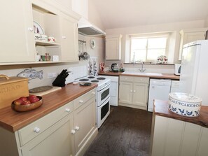 Une cuisine avec des armoires blanches, un plan de travail en bois, une cuisinière, un évier et un réfrigérateur.