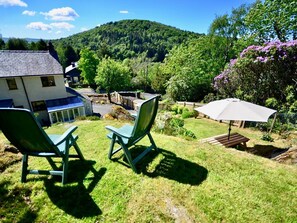A house with a garden, two green chairs, a wooden table, and a white umbrella.