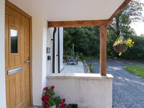 A wooden door, a stone wall, a bench, a hanging flower basket, and a gravel path leading to a house. - Dalegarth Hall Farm Cottage 2. (Holmrook)