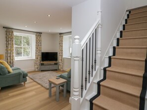 A living room with a sofa, a coffee table, a TV, and a staircase. - Dalegarth Hall Farm Cottage 2. (Holmrook)