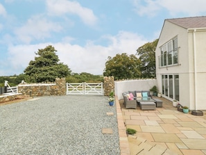 A residential property with a gravel driveway, a stone wall, a white gate, and a patio area with outdoor furniture.