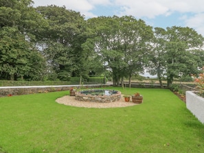 A circular stone water feature surrounded by a gravel bed, with a well-maintained lawn and trees in the background.