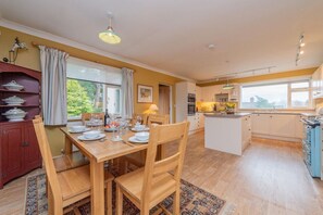 A kitchen with a dining area, wooden chairs, a table set for four, and a view of the outdoors. - Pear Tree Cottage, Pulverbatch (Shrewsbury)
