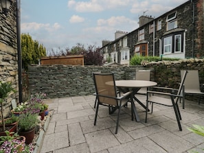 A patio with a round table and chairs, stone walls, and potted plants. - Boundary House, in Windermere. (Windermere)
