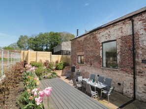An outdoor patio with a brick wall, a wooden deck, and a table set for dining. - Bailey house, Pocklington (Driffield)