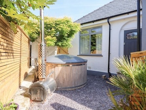 A backyard with a hot tub, a wooden fence, and a house with a window and door. - Trearddur House Cottage, Wales (Holyhead)