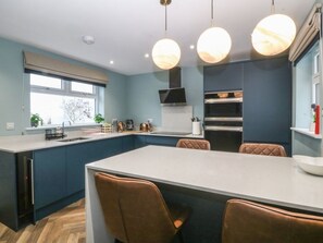 A modern kitchen with a central island, built-in oven, and pendant lighting. - Trearddur House Cottage, Wales (Holyhead)