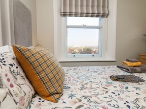 A bedroom with a bed, a window with a view, a bedside table, and a chair.