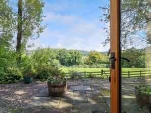 A wooden door leading to a garden with a gravel path, a wooden barrel planter, and a view of a green landscape. - Chapelfield is in Alderwasley. (Belper)