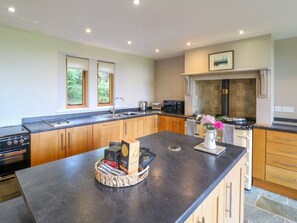 A modern kitchen with wooden cabinets, a black countertop, and a stone fireplace. - Chapelfield is in Alderwasley. (Belper)