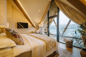 Ein Schlafzimmer mit einem großen Bett, einem Fernseher, einem Fenster mit Vorhängen und Blick ins Freie.