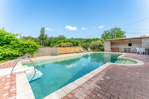 A swimming pool with a wooden deck, a stone wall, and a small outdoor seating area.
