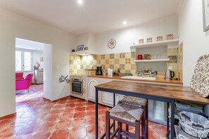 Una cocina con salpicadero de azulejos, cafetera, lavabo y zona de comedor con mesa y sillas.