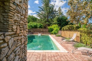 Una piscina de piedra con cubierta de madera, rodeada de follaje y una valla de madera.