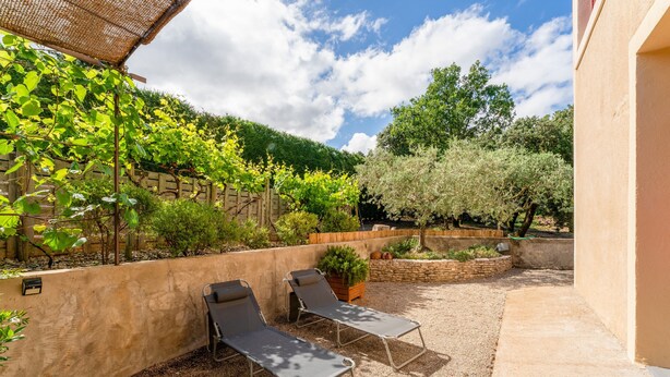 En terrasse med to liggestole, en pergola med slyngplanter og en stenvæg.