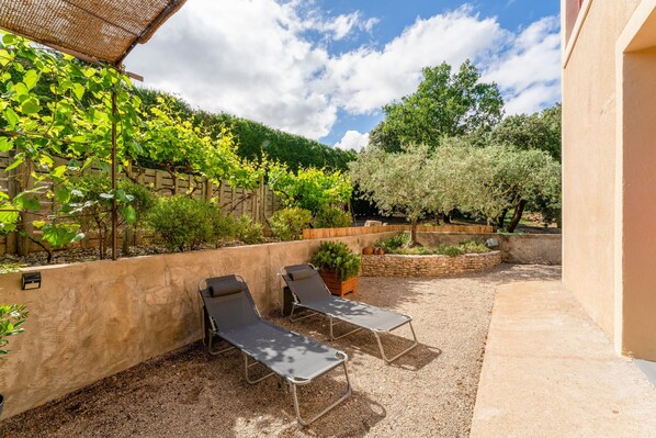 Un patio con dos sillones de descanso, una pérgola cubierta de plantas trepadoras y un muro de piedra.