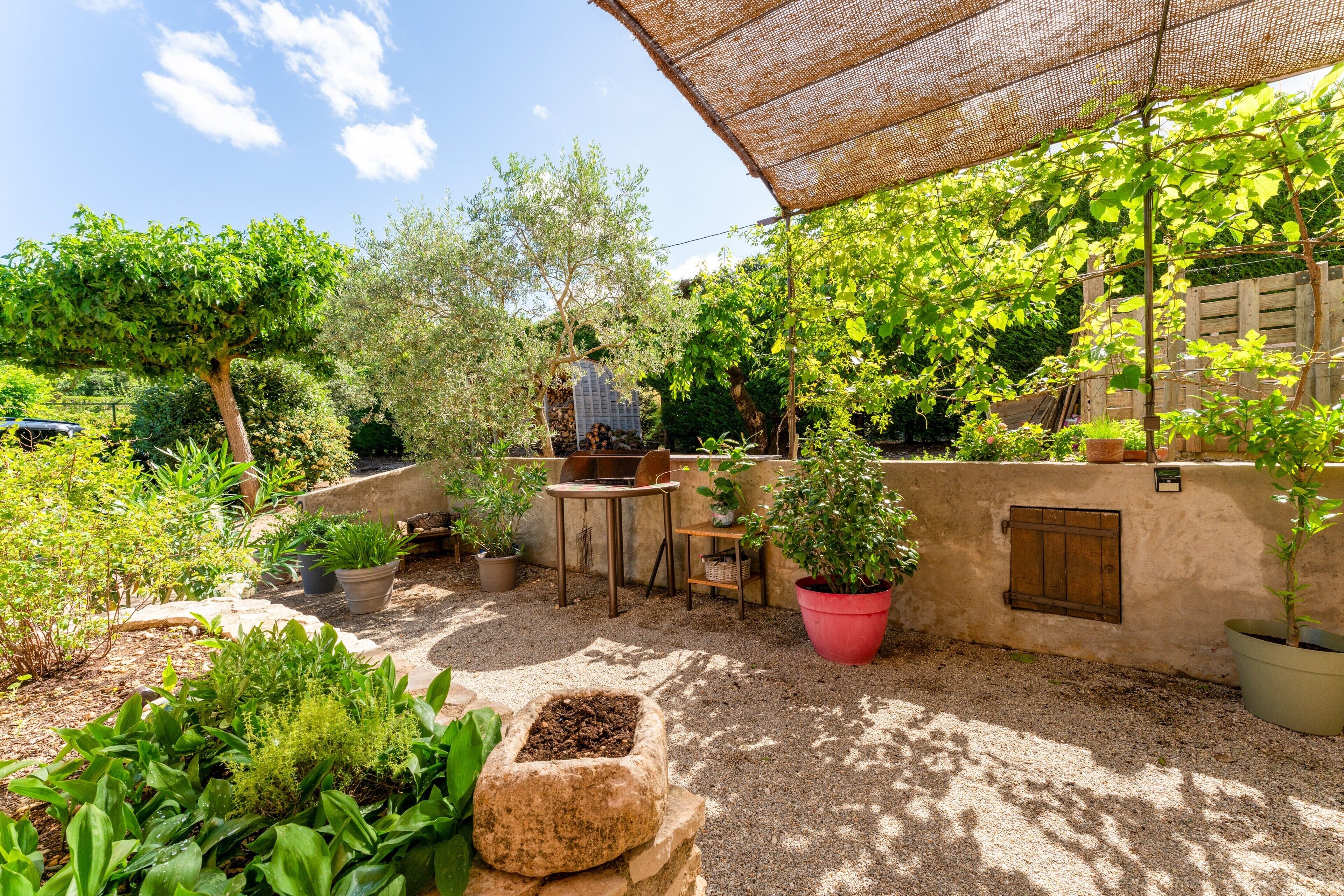 A garden patio with a table and chairs, potted plants, and a pergola.