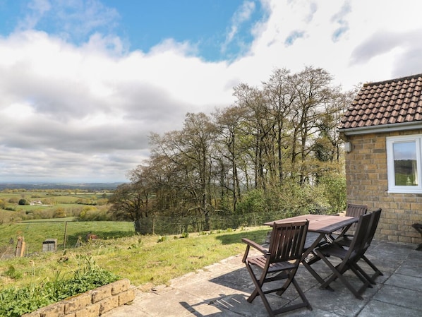 A patio with a table and chairs, a stone wall, and a view of a rural landscape with trees and fields.