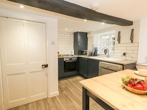 A modern kitchen with dark cabinets, a white countertop, and a wooden table with a fruit bowl.