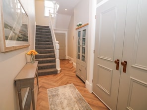 Un pasillo con suelo de madera, una escalera, un armario con puertas de cristal y una puerta con manija.