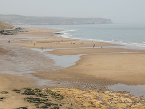Ein Strand mit Menschen, die herumlaufen und stehen, einer felsigen Küstenlinie und fernen Klippen.