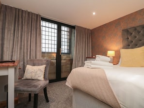 Ein Hotelzimmer mit Bett, Sessel, Schreibtisch und einem Fenster mit Vorhängen.