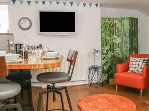 Una sala de estar moderna con una mesa de comedor de madera, sillas negras, un sofá rojo y un televisor grande montado en la pared.
