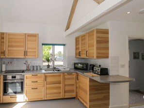 A modern kitchen with wooden cabinets, a built-in oven, a sink, and a window with a view of the outside. - Chapel Cottage, near Pershore. (Pershore)